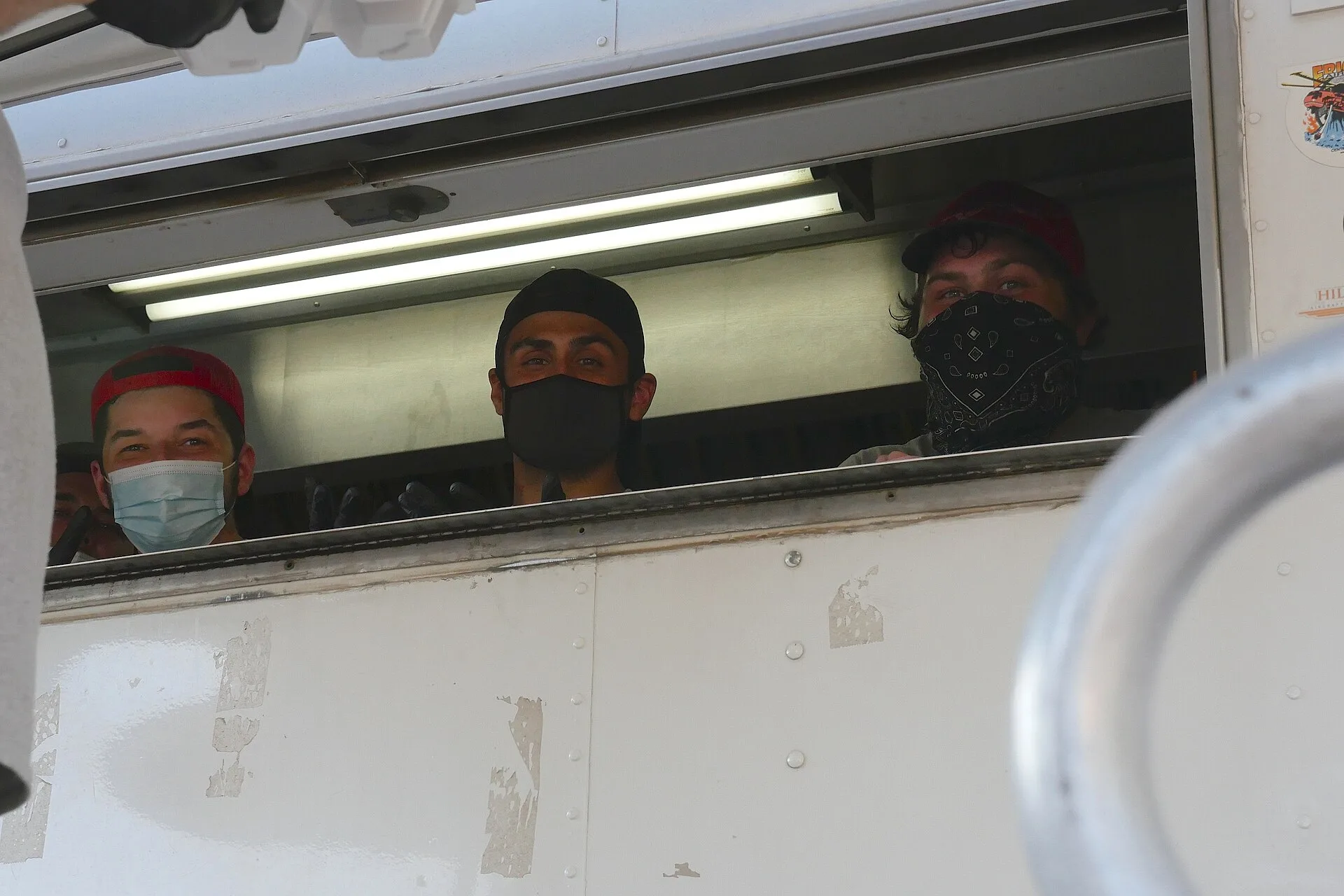 Temperature checks and face coverings are part of daily life in fire camp. Food service workers wear face coverings. Photo depicts three individuals peeking from a window in a food catering truck wearing face coverings. 8.22.2020_RedSalmonComplex_InCamp_SRF_Romney_P1150483 Forest Service photo by Ke. Food truck hiring: build the team around the stations