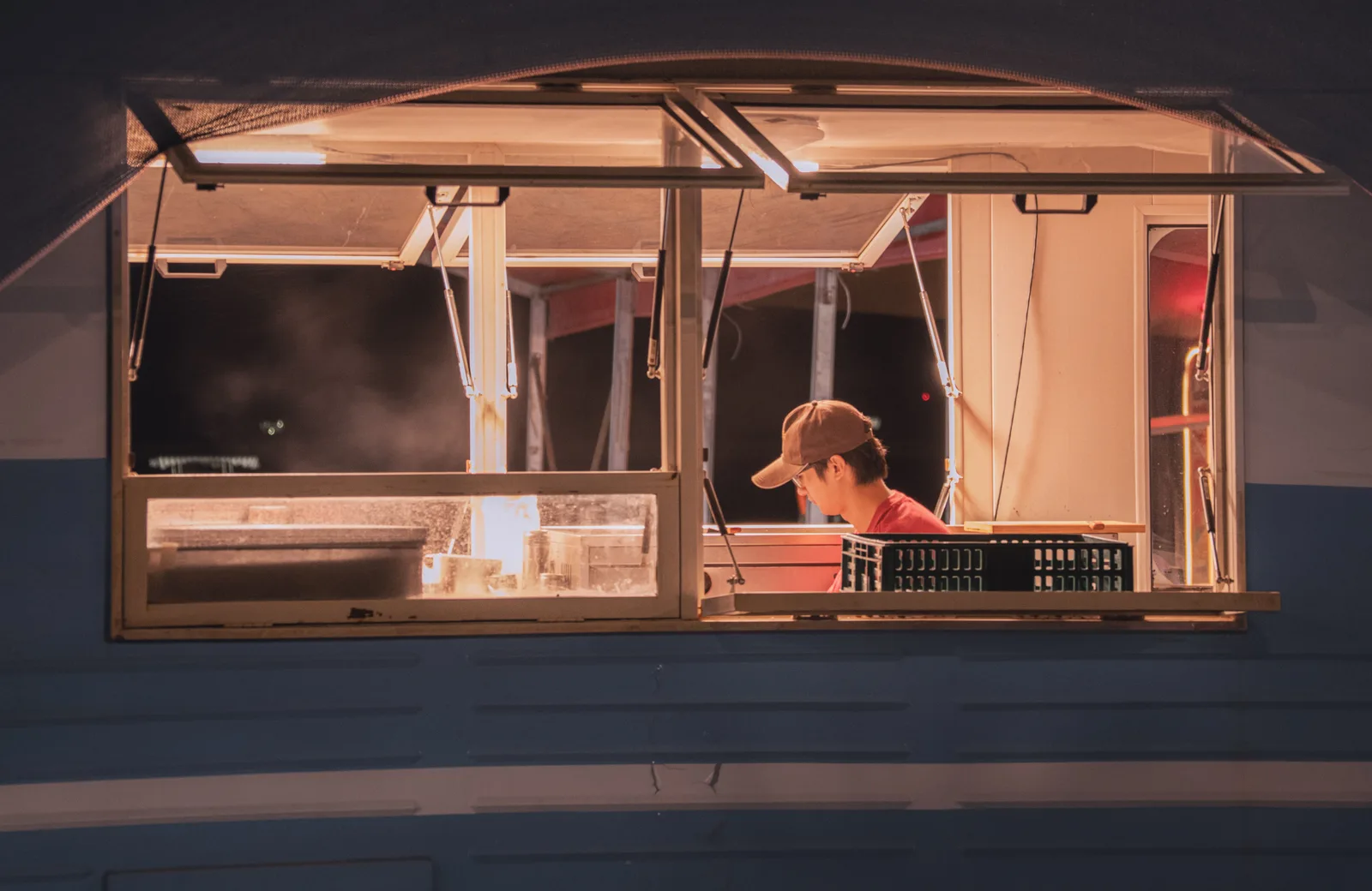 A view of a worker inside a food truck at night, captured through an open window. Food truck profit margin: two formulas to rank each service